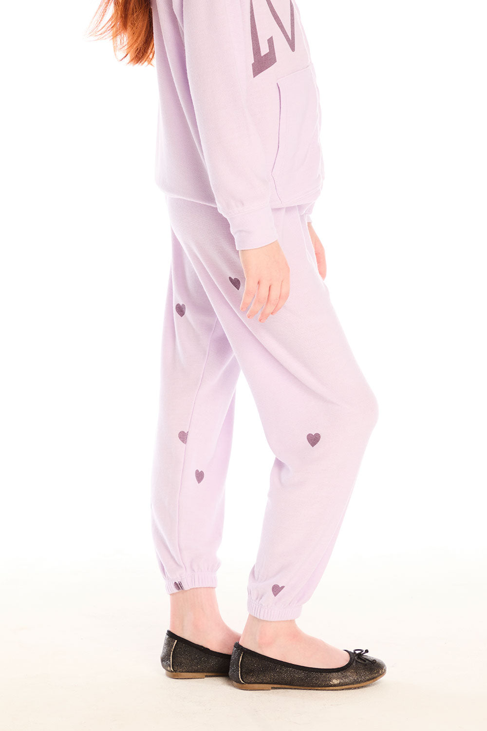Side view of girl wearing Chaser’s pink Love Pants with heart prints on a white background
