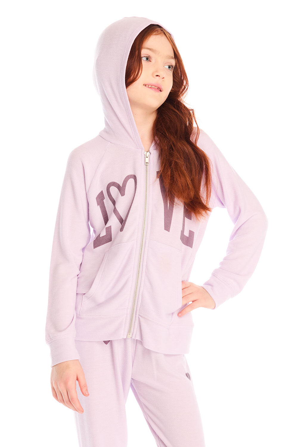 Girl wearing Chaser’s light pink Love Zip Up Hoodie with ‘LOVE’ printed on it and hood up against a white background