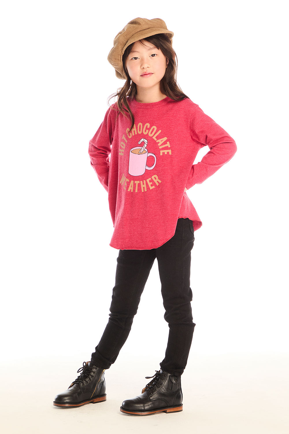 Full body view of girl wearing Chaser’s red Hot Chocolate Weather Long Sleeve with a graphic design, black pants, and a brown hat on a white background