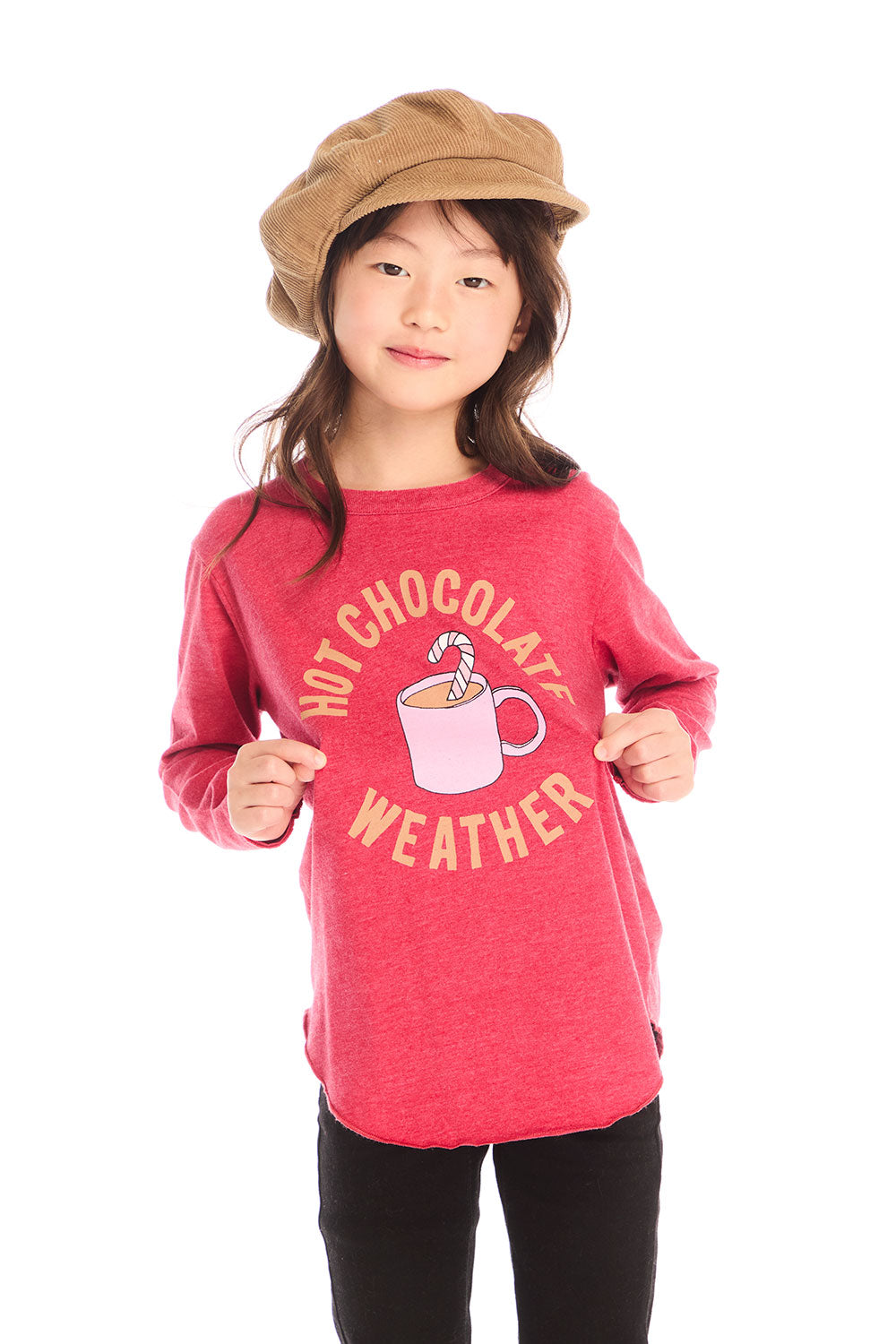 Girl wearing Chaser’s red Hot Chocolate Weather Long Sleeve with a graphic design, black pants, and a brown hat on a white background