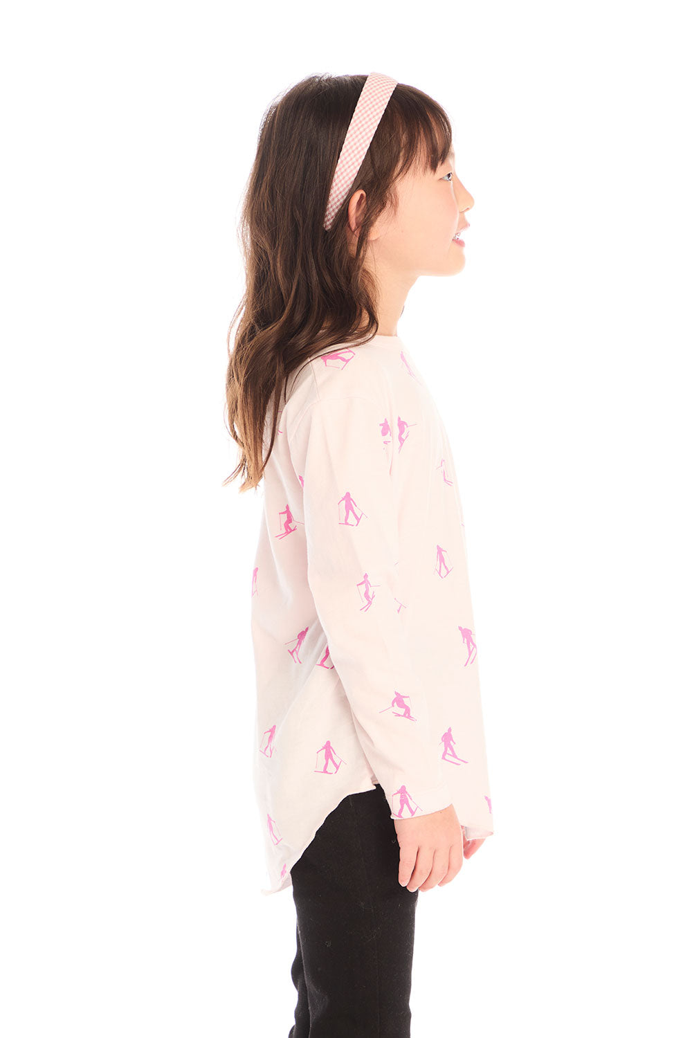 Side view of young girl wearing Chaser’s light pink Allover Pink Skiers long sleeve top with skier patterns on a white background