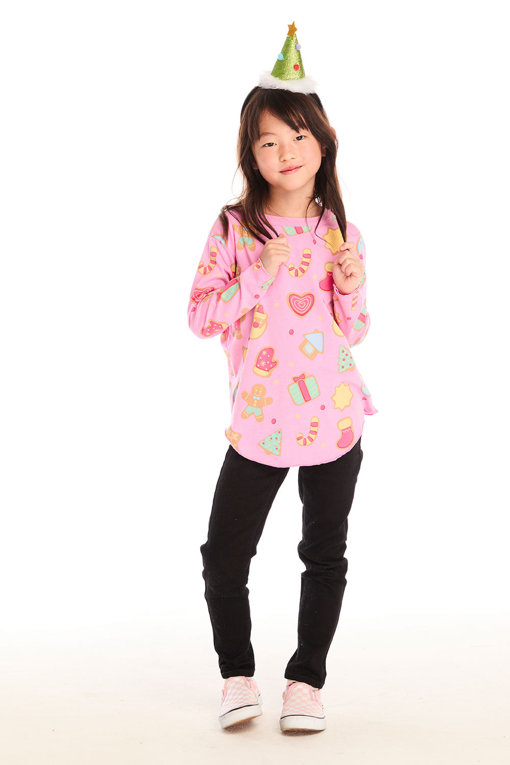 Full body view of girl wearing Chaser’s pink Tossed Candy Canes Long Sleeve with colorful candy cane designs, a Christmas tree hat, and black pants on a white background
