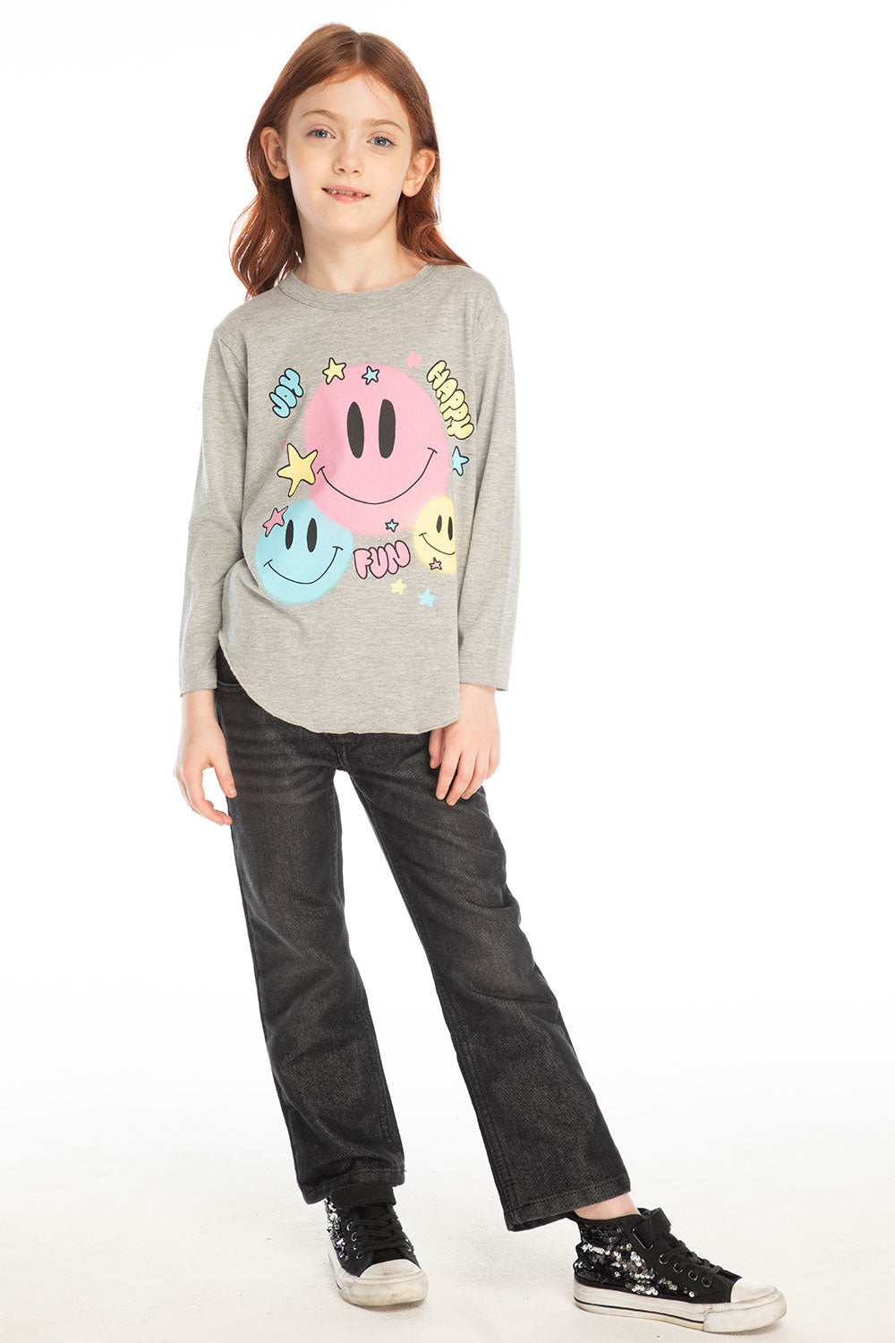 Full body view of girl wearing Chaser’s Heather Grey Colorful Smileys long sleeve pullover with colorful smiley face designs and black jeans on a white background