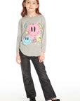 Full body view of girl wearing Chaser’s Heather Grey Colorful Smileys long sleeve pullover with colorful smiley face designs and black jeans on a white background