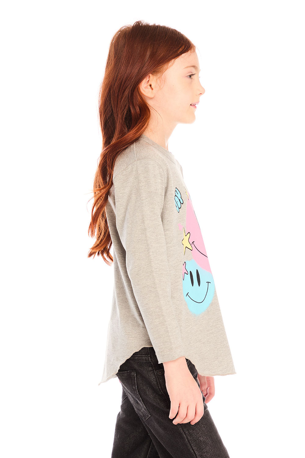 Side view of girl wearing Chaser’s Heather Grey Colorful Smileys long sleeve pullover with colorful smiley face designs and black jeans on a white background
