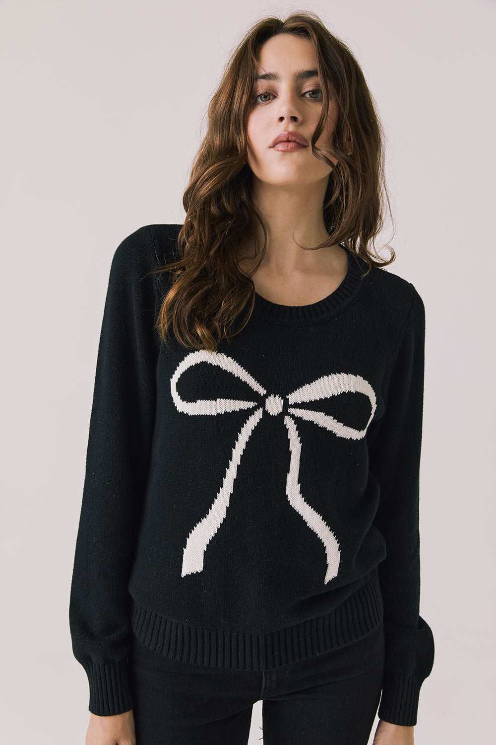 Front view of woman wearing Chaser’s true black Bow Long Sleeve with a white bow design on a plain background.