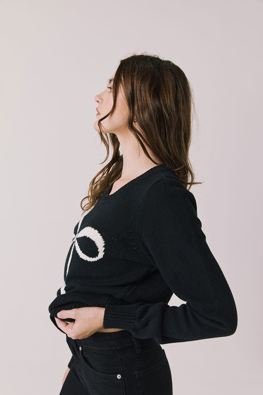 Side view of woman wearing Chaser’s true black Bow Long Sleeve with a visible white bow design on a plain background.