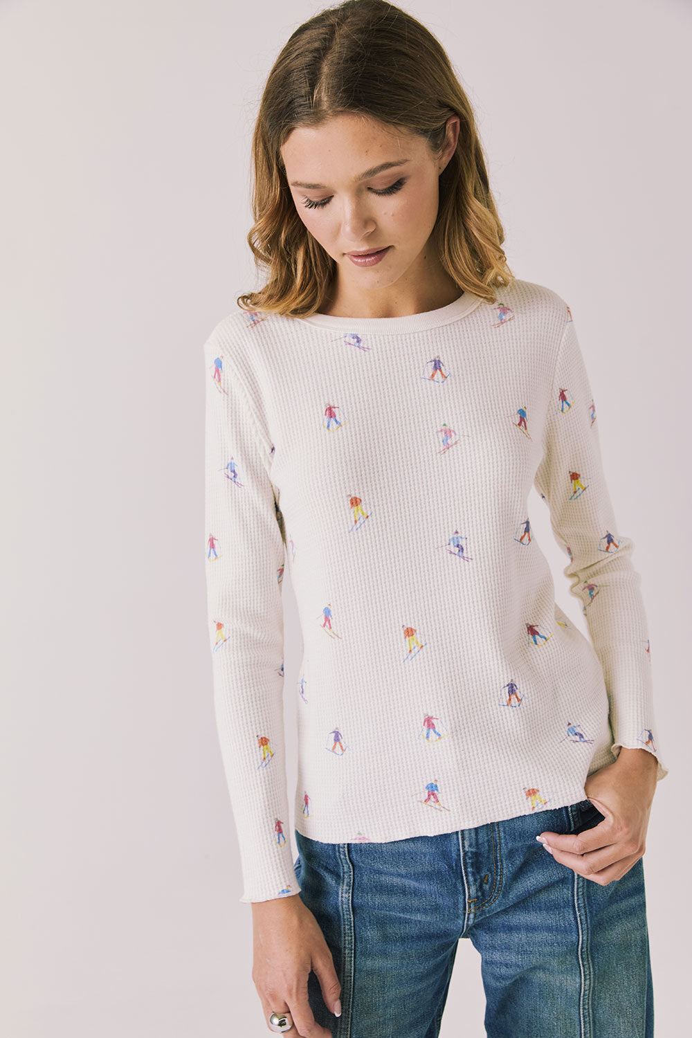 Woman wearing Chaser's Allover Skiers  with small colorful patterns and blue jeans on a light gray background