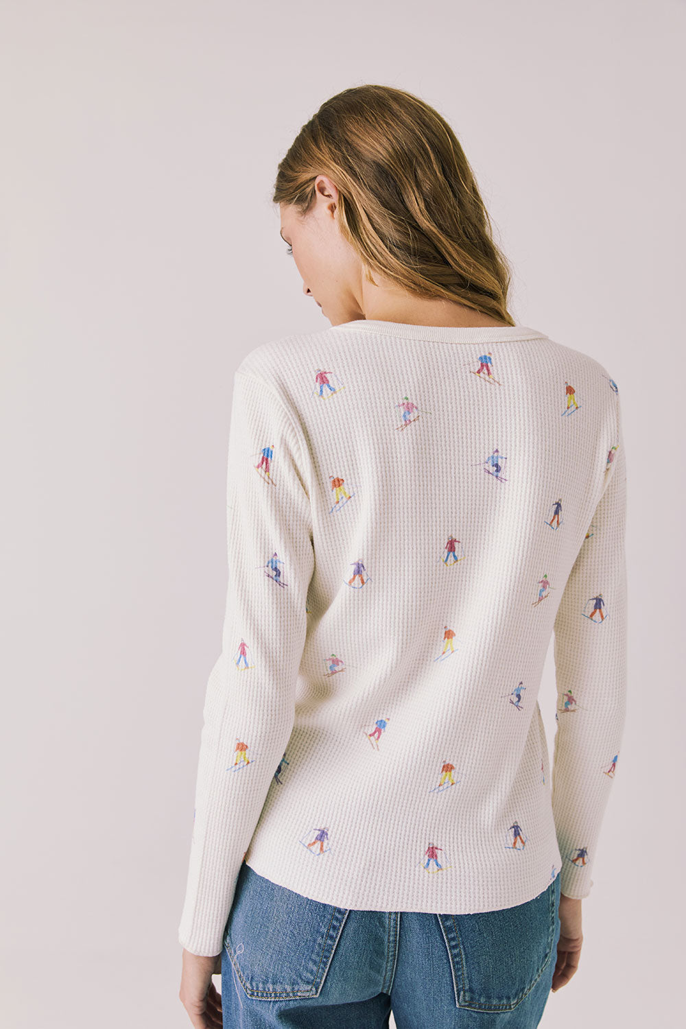 Back view of woman wearing Chaser's Allover Skiers  with small colorful patterns and blue jeans on a light gray background