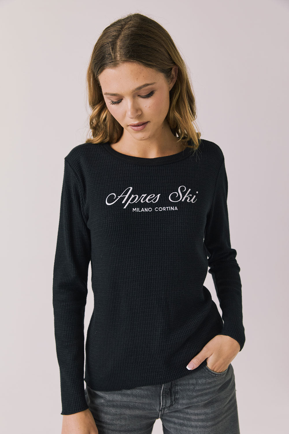 Woman wearing Chaser's black Apres Ski Milano Military Thermal Long Sleeve Tee with 'Apres Ski' text on a plain background