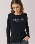 Woman wearing Chaser's black Apres Ski Milano Military Thermal Long Sleeve Tee with 'Apres Ski' text on a plain background