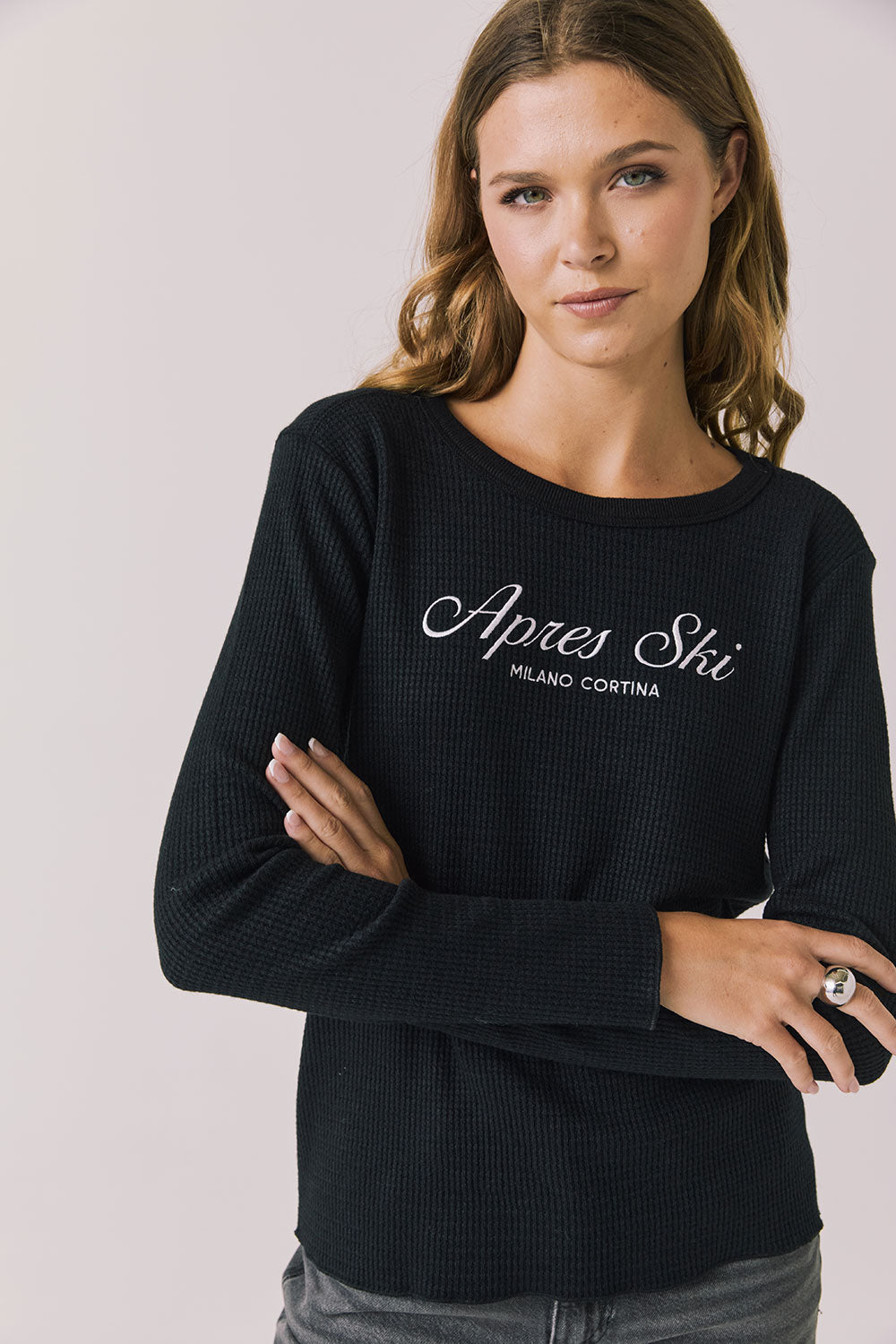 Woman wearing Chaser's black Apres Ski Milano Military Thermal Long Sleeve Tee with 'Apres Ski' text on a plain background