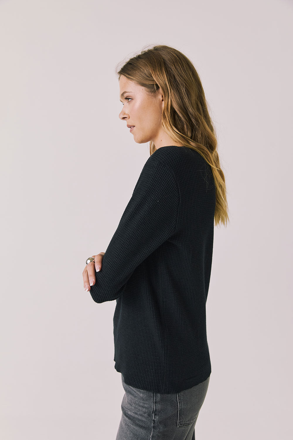 Side view of woman wearing Chaser's black Apres Ski Milano Military Thermal Long Sleeve Tee on a plain background