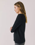 Side view of woman wearing Chaser's black Apres Ski Milano Military Thermal Long Sleeve Tee on a plain background