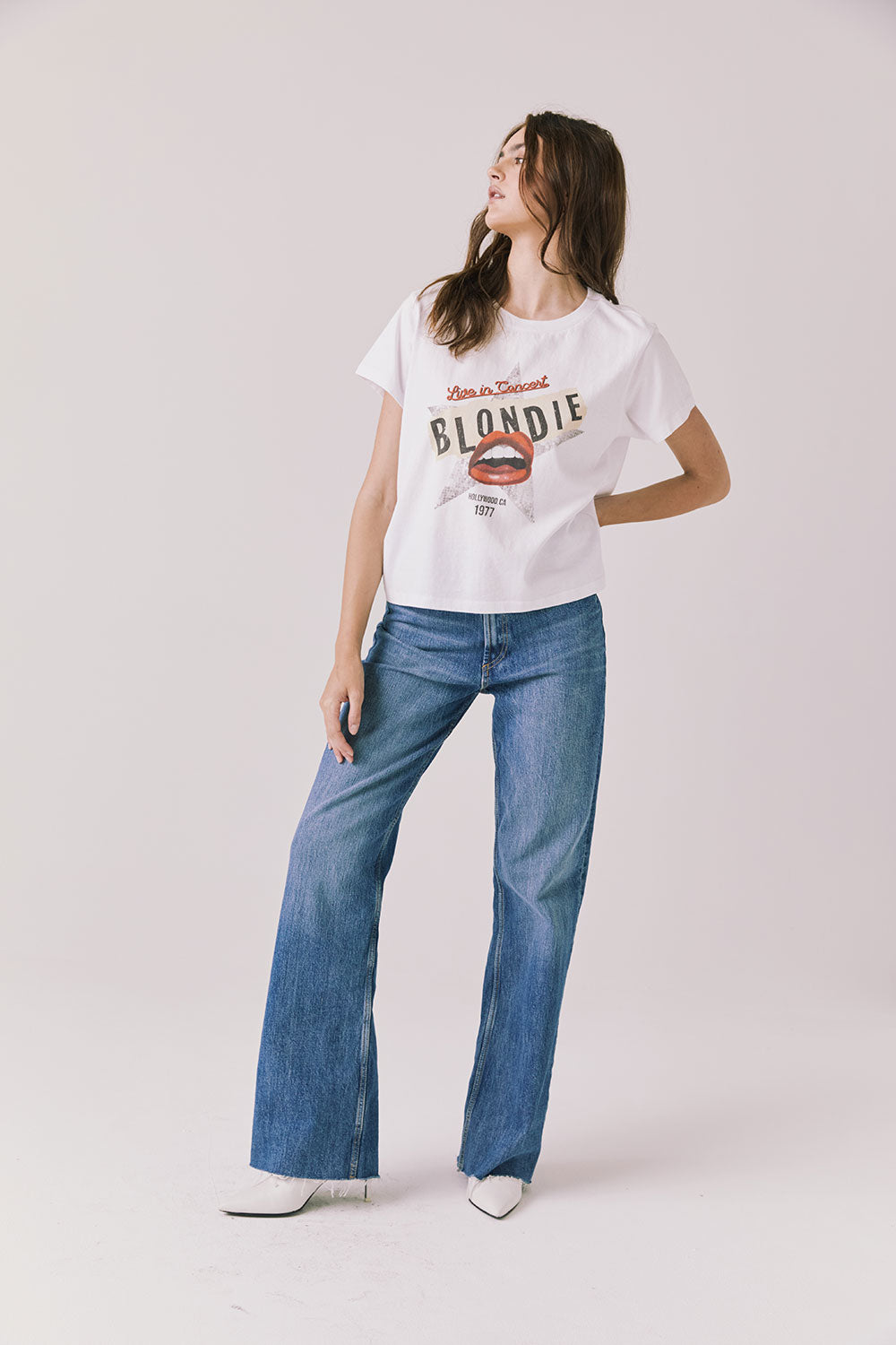 Woman wearing Chaser's white Blondie Live In Hollywood Tee and blue jeans on a plain background