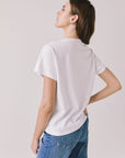 Back view of woman wearing Chaser's white Blondie Live In Hollywood Tee and blue jeans on a plain background