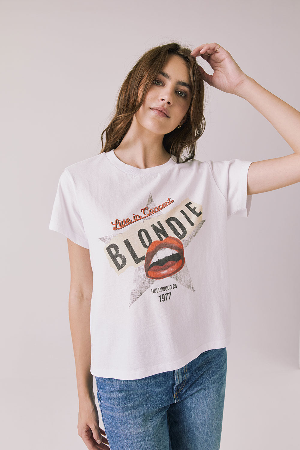 Woman wearing Chaser's white Blondie Live In Hollywood Tee and blue jeans on a plain background