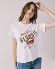 Woman wearing Chaser's white Blondie Live In Hollywood Tee and blue jeans on a plain background