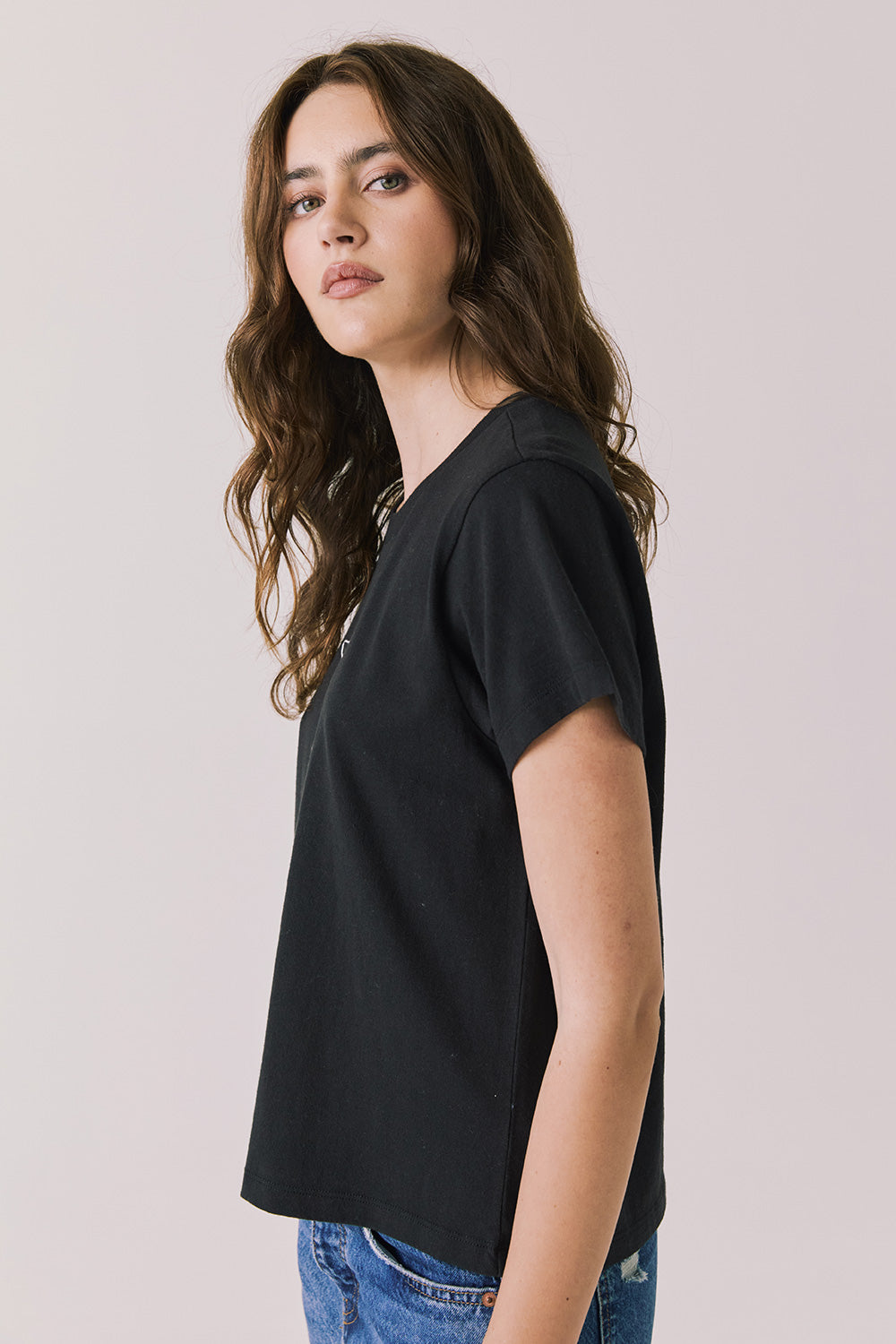 Side view of woman wearing Chaser’s black Tini Time Tee on a plain background