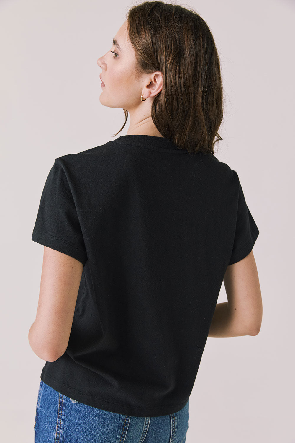 Back view of woman wearing Chaser’s black Tini Time Tee on a plain background