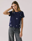 Woman wearing Chaser's Allover Distressed Stars Tee with star patterns and dark denim pants on a plain background