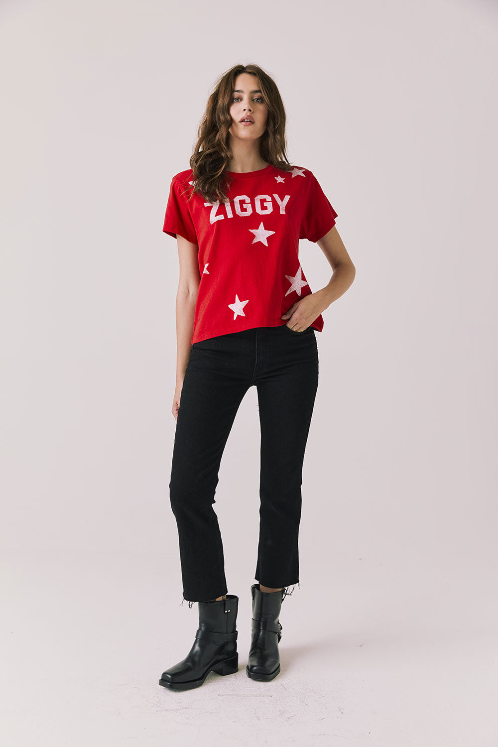 Full body view of woman wearing Chaser’s Rouge Red David Bowie Ziggy Stardust Tee with black jeans and black boots on a light gray background (Licensed band collaboration — features official David Bowie branding for SEO relevance)