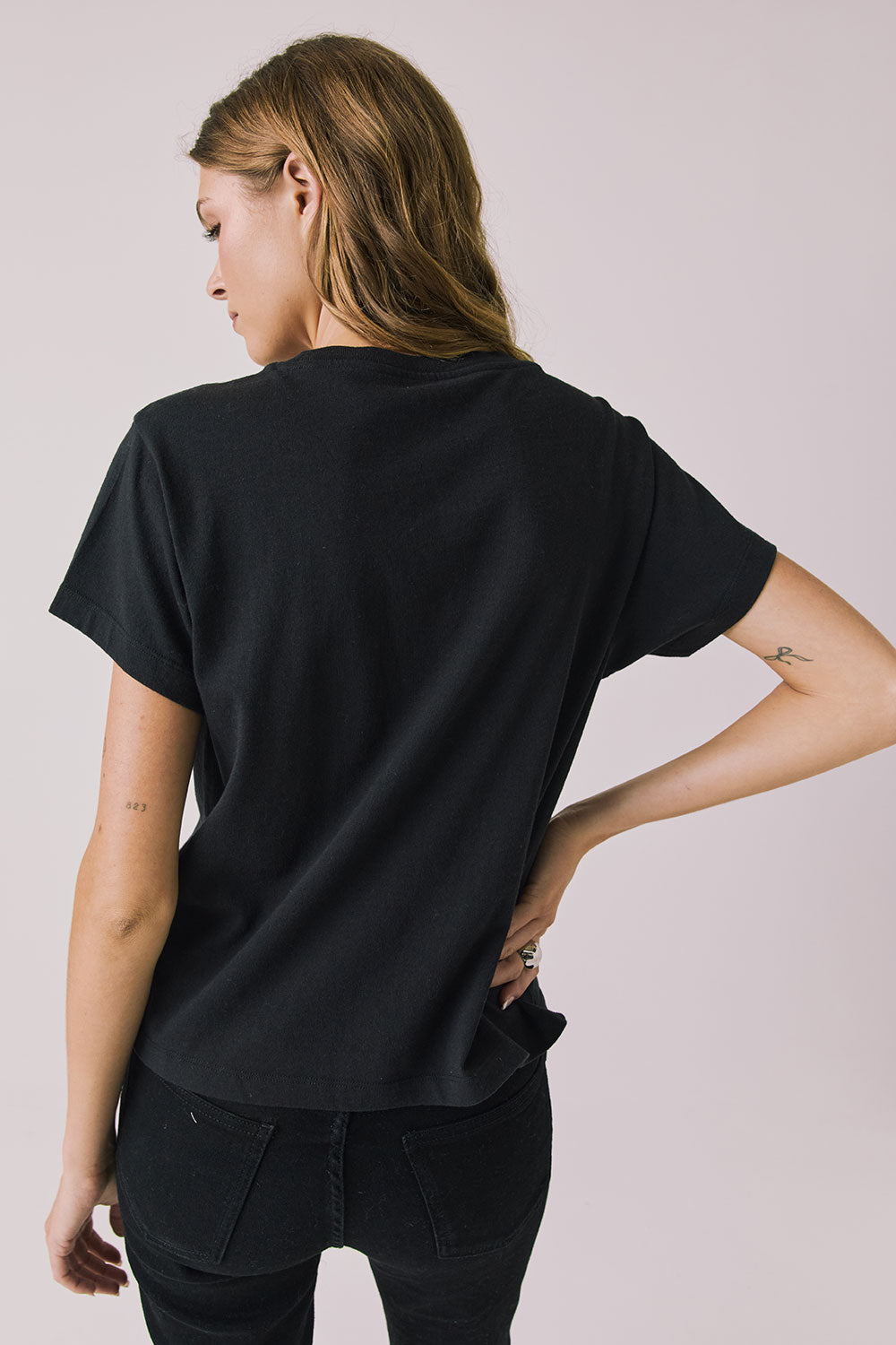 Back view of woman wearing Chaser’s The Rolling Stones The British Are Coming Tee in True Black on a plain background