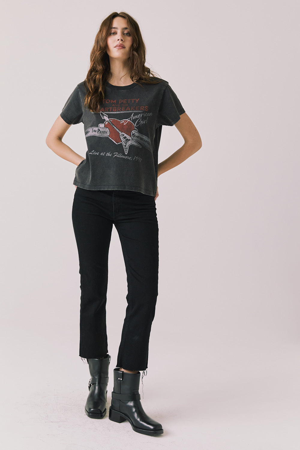 Full body view of woman wearing Chaser’s Tom Petty Live At The Fillmore Tee with black pants and boots on a plain background