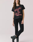 Full body view of woman wearing Chaser’s Whiskey A Go Go Classic Neon Logo black Tee with red text, black pants, and black boots on a light background