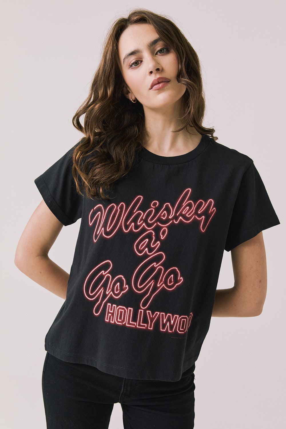 Front view of woman wearing Chaser’s Whiskey A Go Go Classic Neon Logo black Tee with red neon-style text on a light background