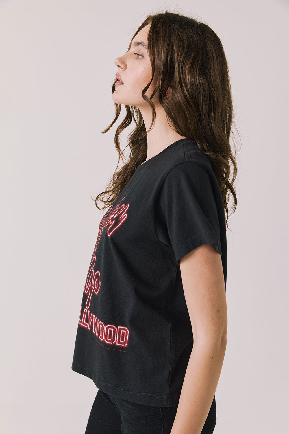 Side view of woman wearing Chaser’s Whiskey A Go Go Classic Neon Logo black Tee with red graphic text on a light background