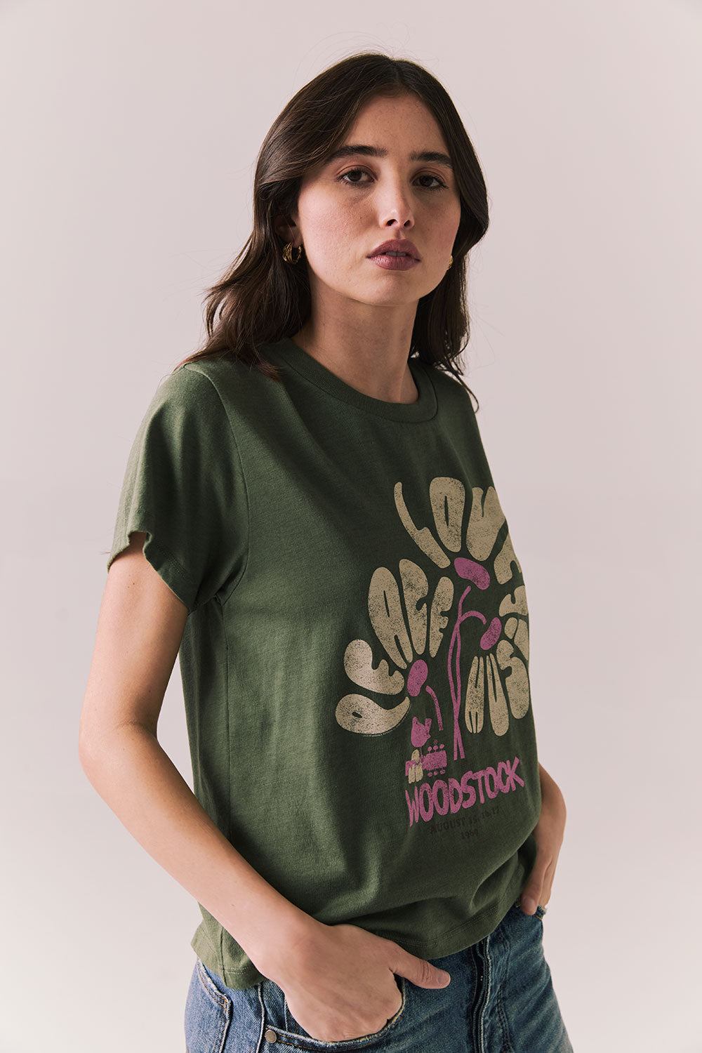 Side view of model wearing Woodstock Festival Flower Tee in bronze green with cream and pink floral graphic and vintage font against a plain background