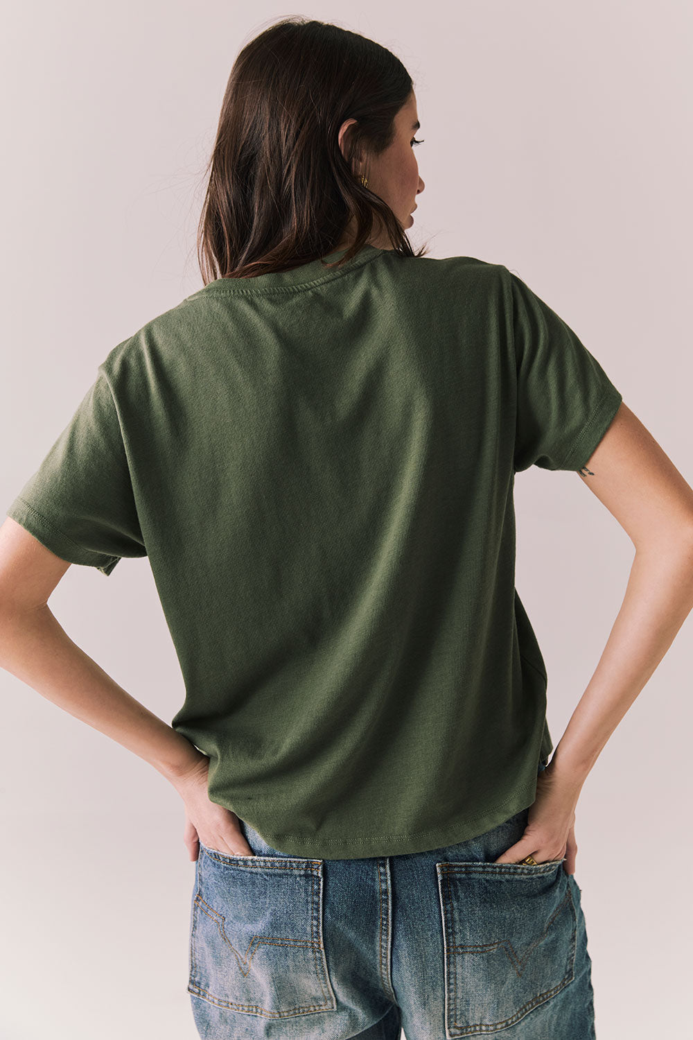 Back view of model wearing Woodstock Festival Flower Tee in bronze green against a plain background