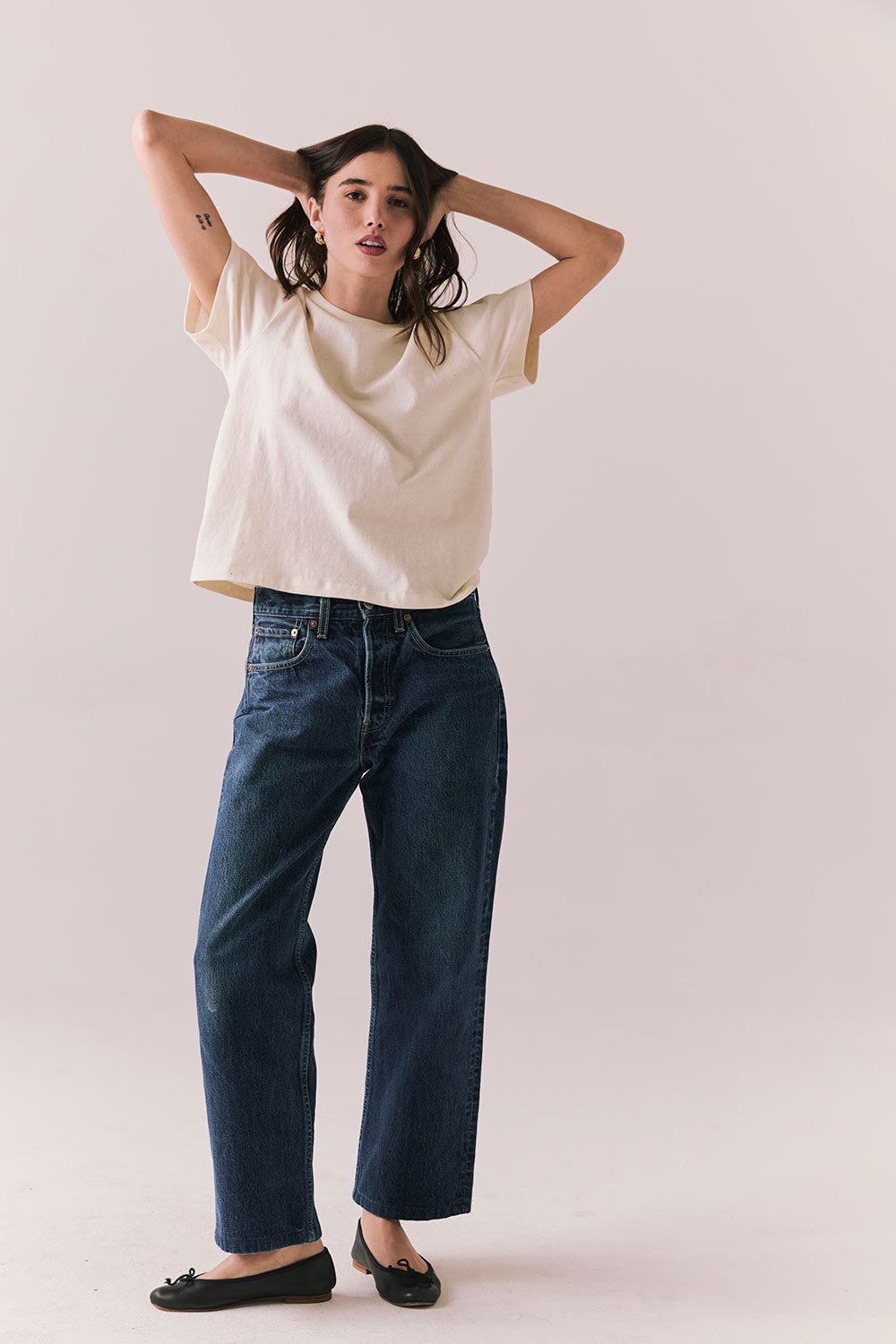 Woman standing against a plain background wearing the Rambler Starry White Tee with ringer neck and cap sleeves and blue jeans