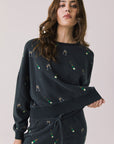 Front view of woman wearing Chaser’s black Champagne Party Long Sleeve Pullover with allover champagne bottle and glass graphics on a light grey background