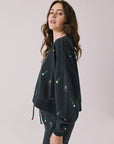Side view of woman wearing Chaser’s black Champagne Party Long Sleeve Pullover with allover champagne bottle and glass graphics on a light grey background