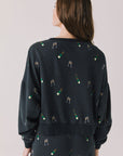Back view of woman wearing Chaser’s black Champagne Party Long Sleeve Pullover with allover champagne bottle and glass graphics on a light grey background