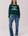 Full body view of woman wearing Chaser’s Blue Grass Green C’est Le Weekend Long Sleeve with blue jeans on a plain background