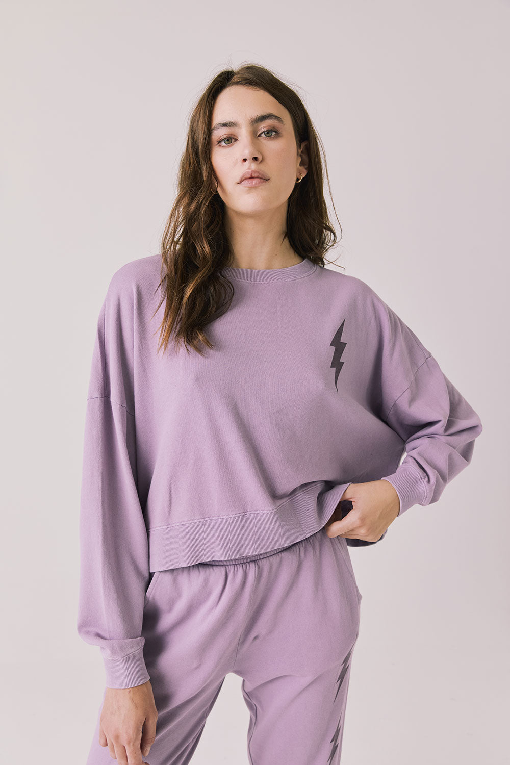 Woman wearing Chaser’s Bolt Amethyst Purple Pullover with matching joggers on a plain background