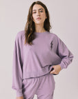 Woman wearing Chaser’s Bolt Amethyst Purple Pullover with matching joggers on a plain background
