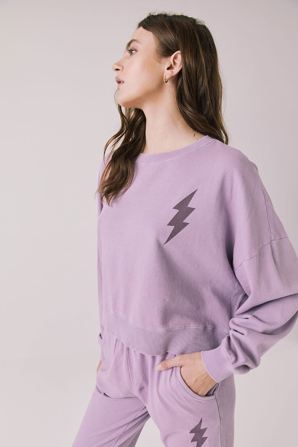 Side view of woman wearing Chaser’s Bolt Amethyst Purple Pullover with matching joggers on a plain background