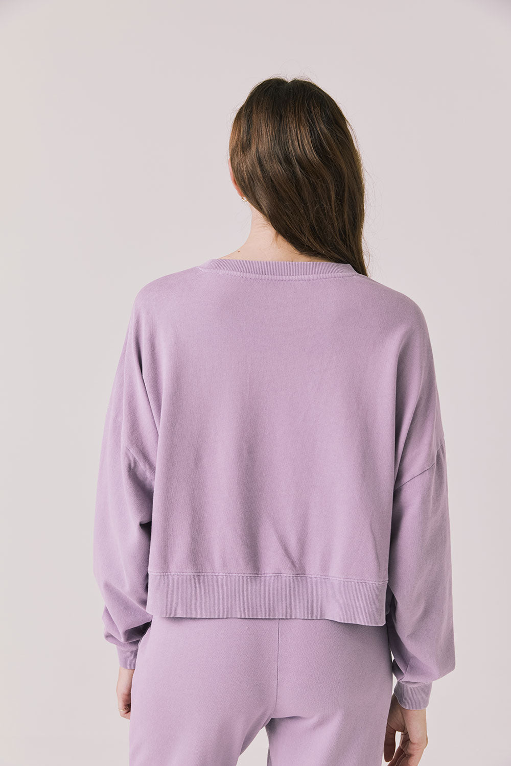 Back view of woman wearing Chaser’s Bolt Amethyst Purple Pullover with matching joggers on a plain background