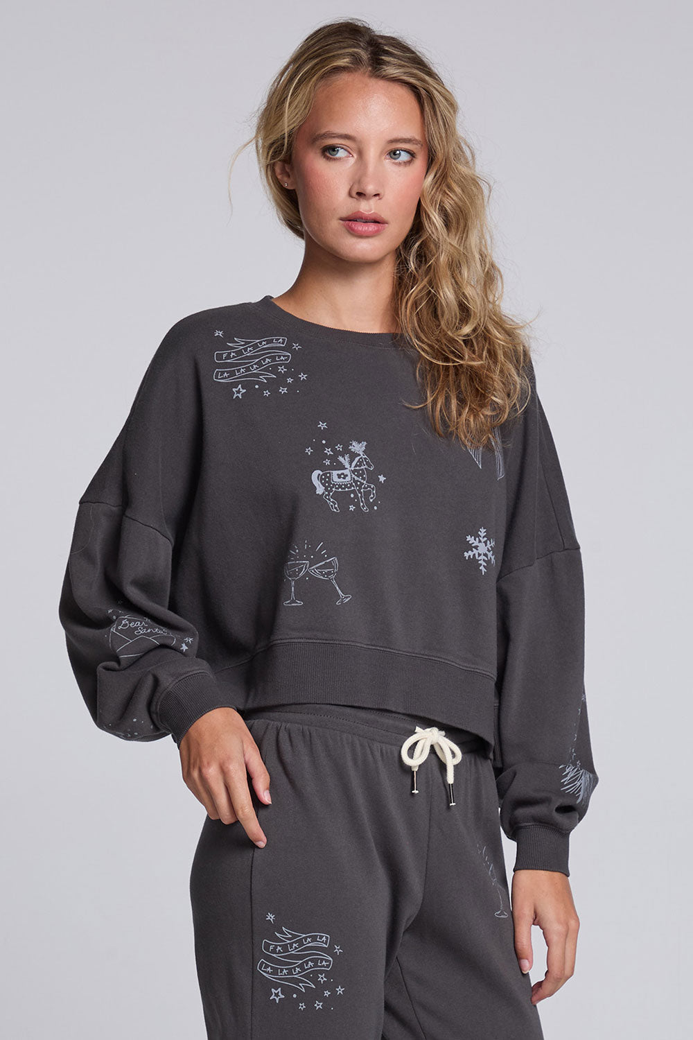 Model wearing Chaser's Holiday Cheer Pullover in Fresh Gravel with scattered holiday icons, angled view