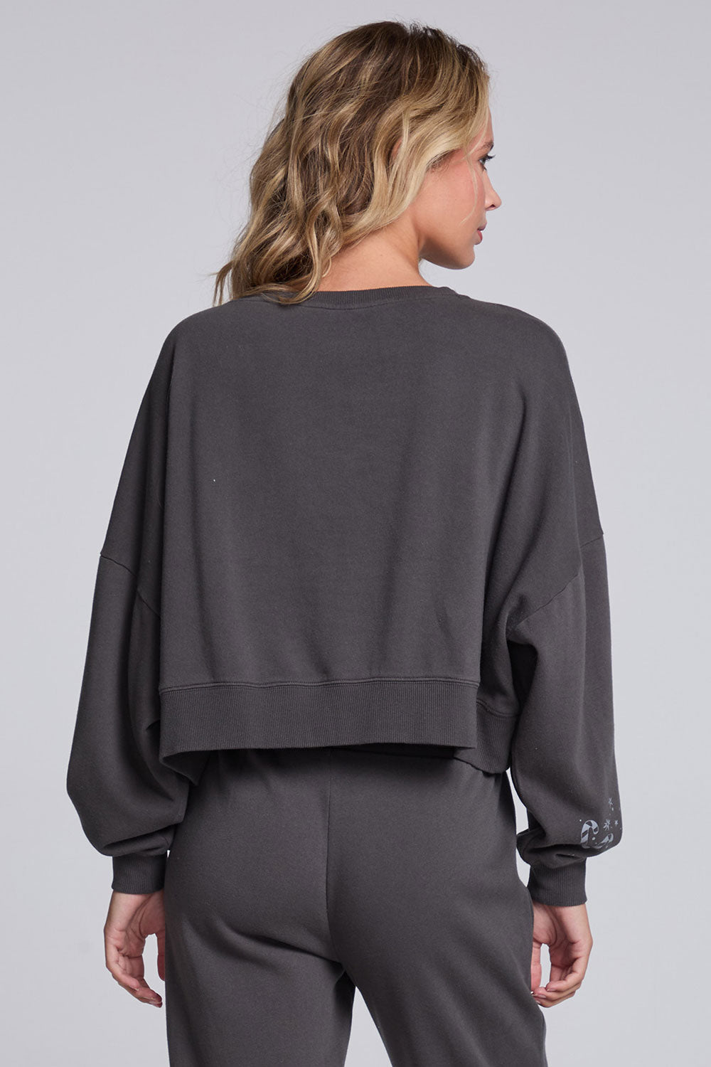 Model wearing Chaser's Holiday Cheer Pullover in Fresh Gravel with scattered holiday icons, back view