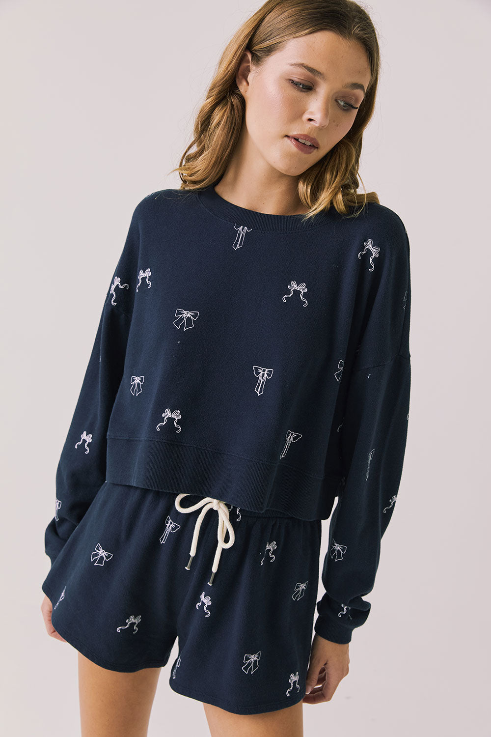 Front view of woman wearing Chaser’s navy Tossed Bows Long Sleeve with small bow prints on a white background