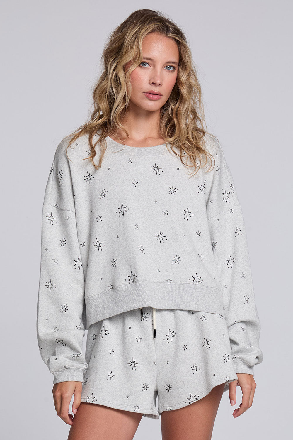 Model wearing Chaser's Twilight Pullover in Heather Grey with scattered black stars and spark details, front view