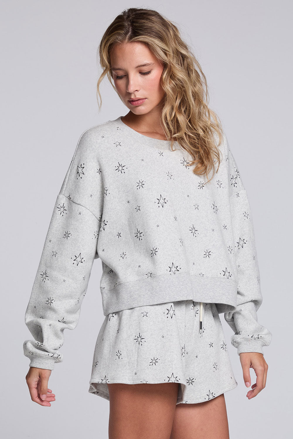 Model wearing Chaser's Twilight Pullover in Heather Grey with scattered black stars and spark details, angled view