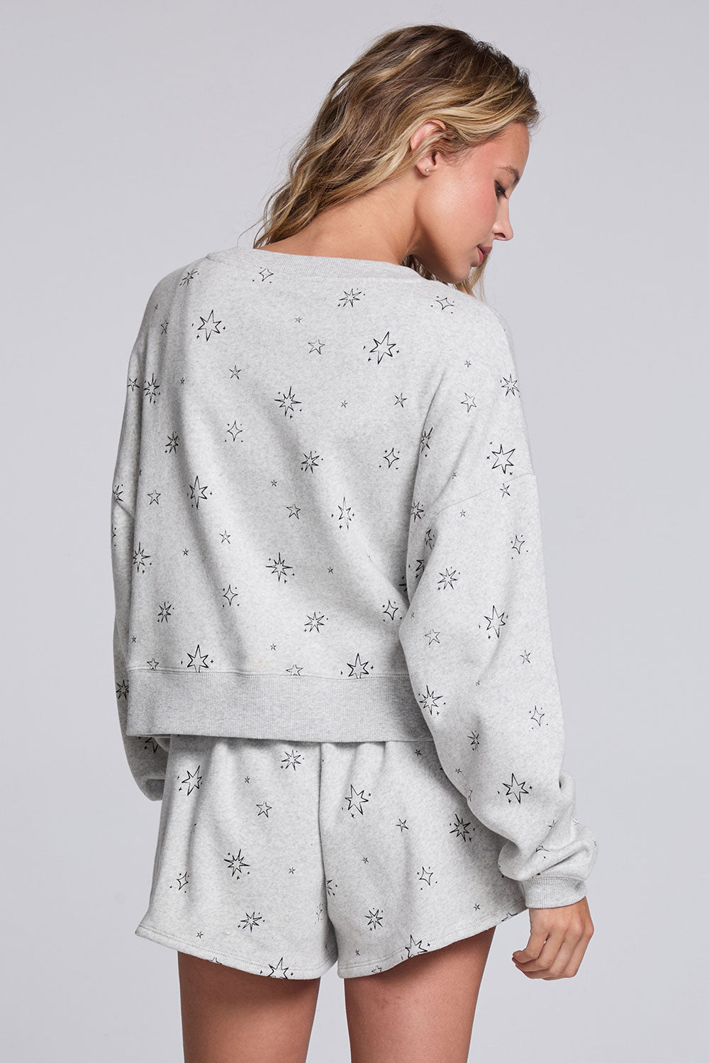 Model wearing Chaser's Twilight Pullover in Heather Grey with scattered black stars and spark details, back view
