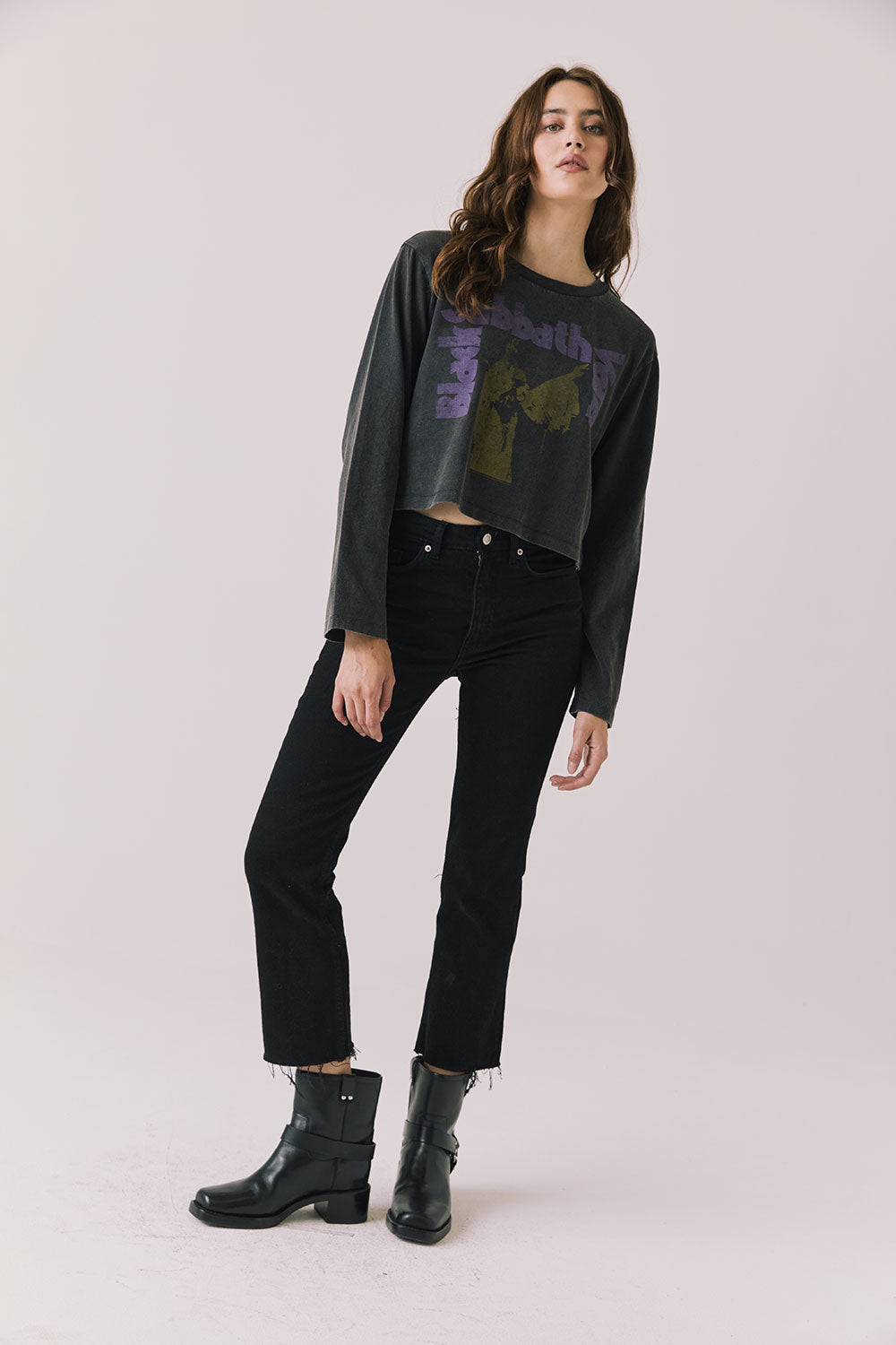 Woman wearing Chaser's black oversized Black Sabbath Vol 4 Long Sleeve top with a graphic design, black pants, and black boots on a white background