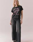 Woman wearing Blondie Heart of Glass tee in black with a graphic design and text, paired with dark jeans on a plain background